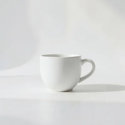 Minimalist photography of a single white coffee cup on a clean matte surface, soft natural window light, subtle shadow, 