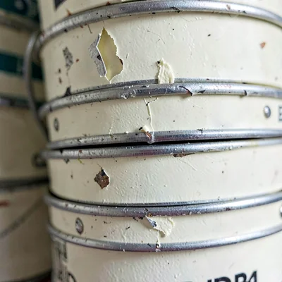 Vertical detail of a stack of dented film cans with peeling cream paint