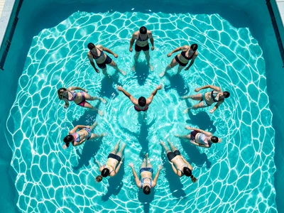 A water aerobics class from above, a dozen people in a circle in a pool, the ins