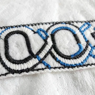 Embroidered panel macro — C and U curve forms interlocking in black thread on wh
