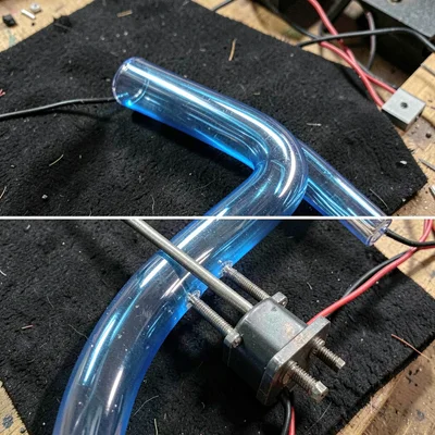 A finished section of bent glass tube in blue against a black felt backing, clos