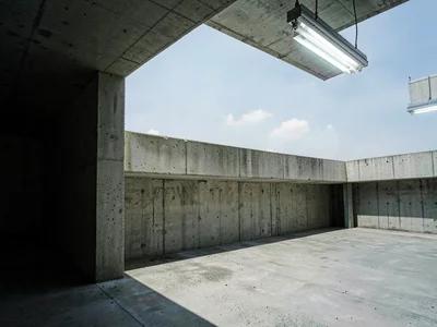 A car park top level — raw concrete balustrade, open sky beyond, deep shadow in 