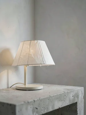 Side profile of a paper-shade lamp on chalky concrete, soft sidelight emphasizin