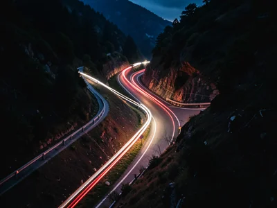 Car light trails on mountain switchback road from above, red and white streams