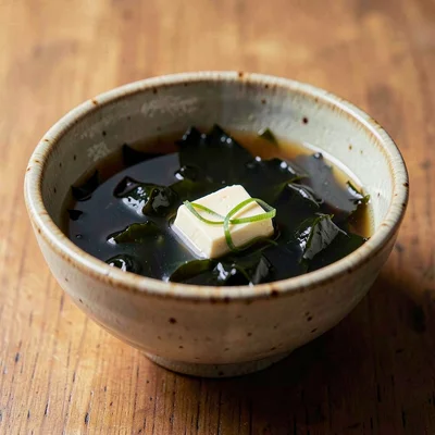 Hand-thrown ceramic bowl of dark seaweed broth with a single tofu cube floating