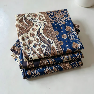 A folded stack of finished batik cloth in indigo, brown, and cream, shot overhea