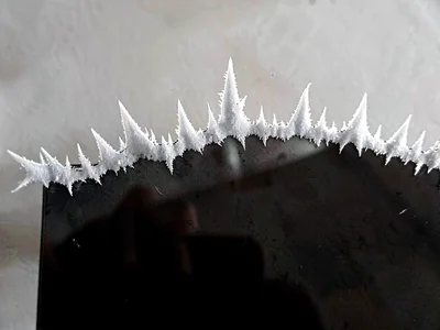 Hoar-fringe ridge running across the upper edge of a cold black glass plate, eve