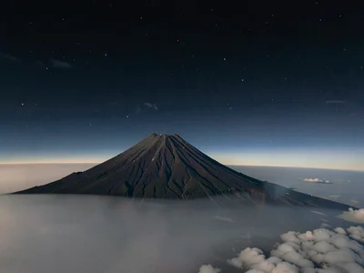 Volcanic peak rising above inversion layer into clear dark upper atmosphere
