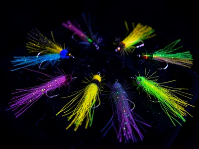 A fishing lure collection arranged on black cloth under UV — synthetic fibers gl