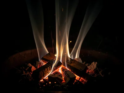 A campfire ember bed with heat shimmer columns dancing above glowing coals