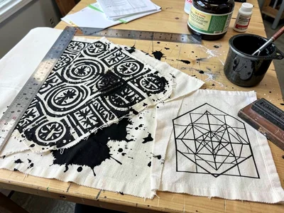 Cloth in progress on stamping table — ruler, stamp, dye pot, half-stamped fabric
