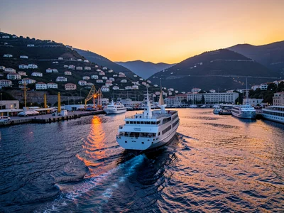 A white ferry pulling away from a Greek island dock at sunset, the wake in orang