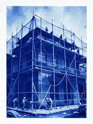 A scaffolded building wrapped in construction mesh with workers visible behind i