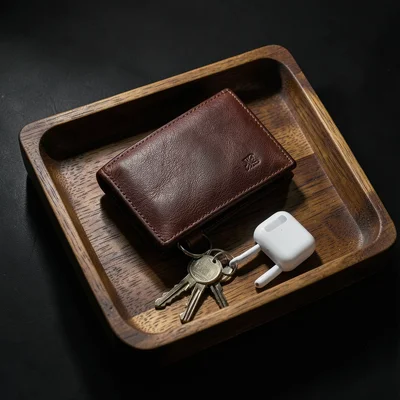 Leather wallet, keys, and AirPods arranged on a wooden tray, everyday carry flat