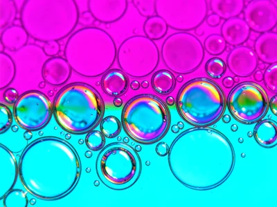 Oil dispersal on water with half magenta half cyan background, bubbles showing s
