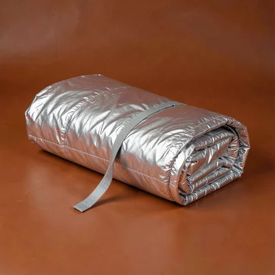 single rolled aluminium portable picnic-blanket at three-quarter angle on a satu