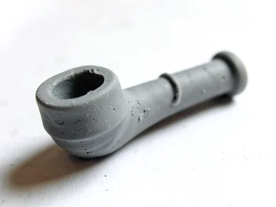 Newly-fired putty-grey clay pipe with a slumped bowl and thumb dents along the s