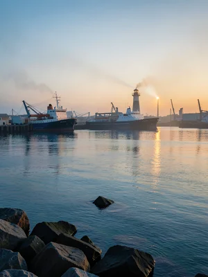 A lighthouse at dawn, the beam still visible in morning mist, the sea calm, rock