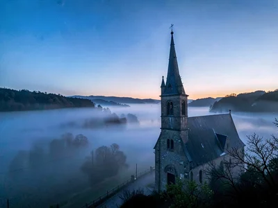 Church spire rising above fog sea catching first light