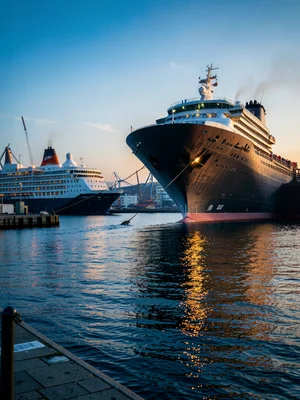 A cruise ship seen from the dock, the massive hull curving upward, tiny passenge