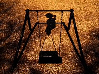 The shadow of a playground swing set cast onto wood chip ground cover at golden 