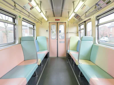 Pastel-colored train car interior, symmetrical seats, center aisle, luggage rack