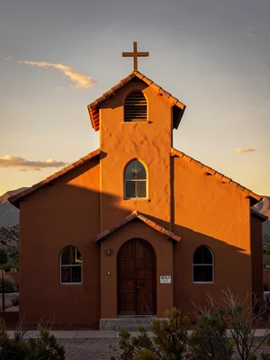 Adobe church in New Mexico light, walls turned pumpkin orange, shadows gone purp