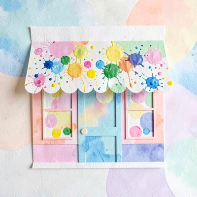 Playful cut-paper scene of an art-studio storefront with paint-splatter awning, 