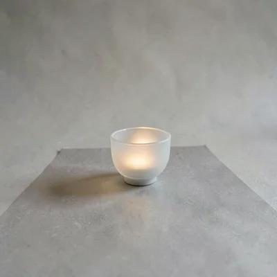A small porcelain teacup placed off-center on warm-grey paper, translucent walls