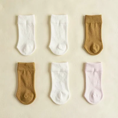 Color-block grid flatlay of six folded socks tubes in alternating cream and must