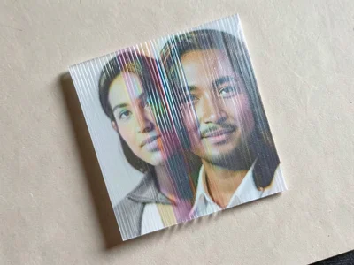 Lenticular card mid-tilt, image A dissolving into image B through progressive st