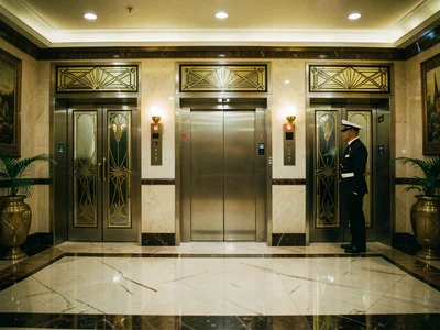 A hotel elevator lobby, three elevators with art deco doors, a bellhop waiting, 