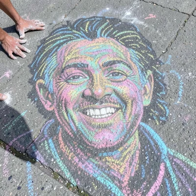 A massive street chalk portrait, the artist's chalk-dusty hands visible at the e