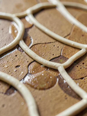Razor-sharp focus on slip-trailed cream loops over toasted stoneware, raised lin