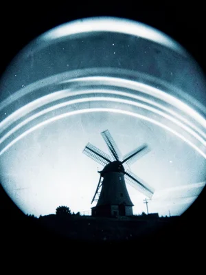 A hilltop windmill, sails blurred by long exposure, sun arcs crossing above