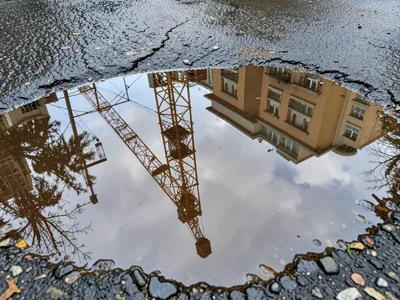 Construction crane reflected in muddy puddle on job site, geometric industrial s