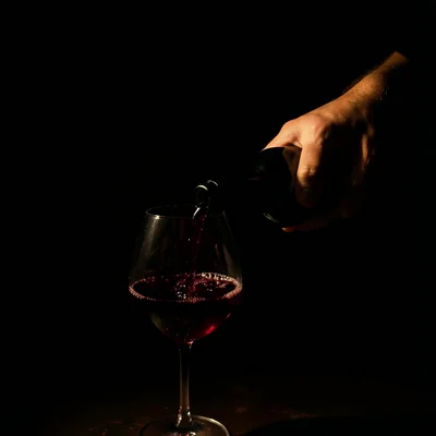 A hand pouring red wine from a bottle into a glass, the liquid catching light li