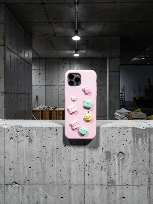 Pastel phone case with cute charms on concrete barrier, construction site backgr
