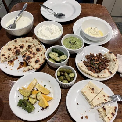 Breakfast table with multiple dishes overlapping, flatbread torn apart, yogurt b