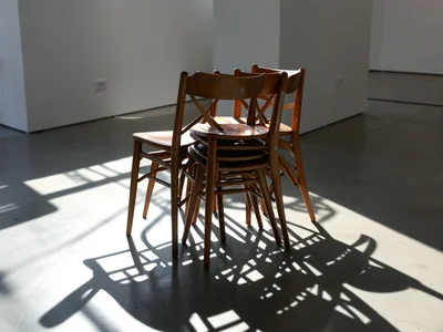 Stacked chairs creating intricate shadow pattern on floor, afternoon light, gall