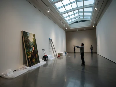 A gallery during installation: a painting leaning against the wall, ladder, bubb