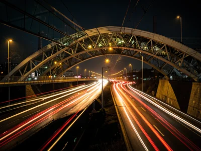 Bridge arch containing rush hour traffic light trails at night, double exposure