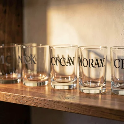 Warm still-life of a row of nick-and-norah glasses on a wooden shelf, soft tungs