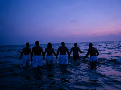 The last swimmers of the day emerging from the ocean at blue hour, their silhoue