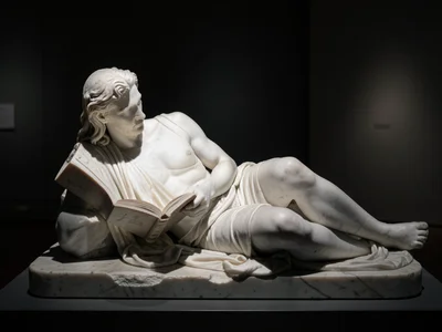 A reclining figure reading a book, carved in white marble, the book pages so thi