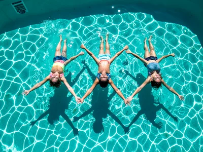 Three children floating on their backs in a turquoise pool, arms out in star sha