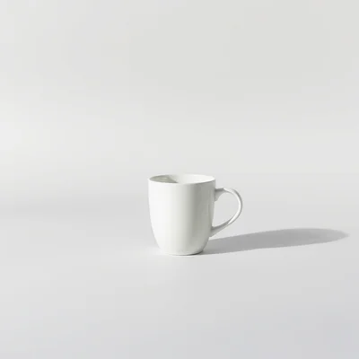 Minimalist studio photograph of a single white coffee cup on a seamless pale gray background, soft natural light, subtle