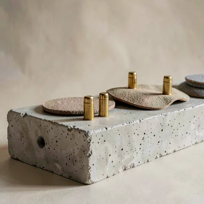 Sculptural lineup of slip-mats and brass cartridges on a chalky concrete plinth