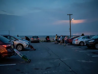 Beach parking lot half-empty, families loading sandy equipment into cars