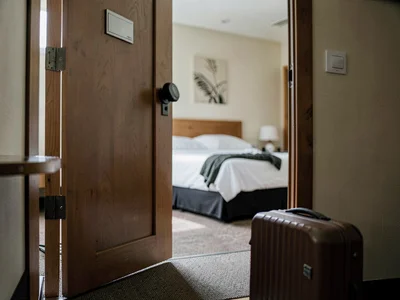 Hotel room door held open with a foot, suitcase ready, one last look at the unma